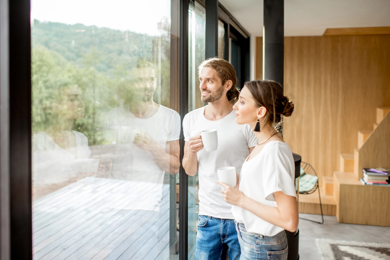 Zwei Personen betrachten gemeinsam eine moderne Wohnung mit bodentiefen Fenstern, die sie bei meinfenster24.de gekauft haben.