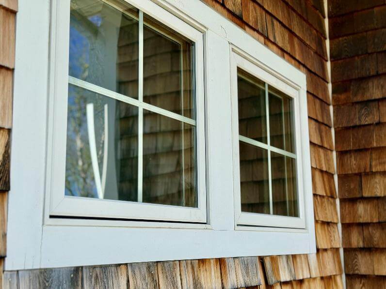Nahaufnahme eines Fensters mit weißen Holzrahmen und rechteckigen Gittern, eingebettet in eine Holzfassade