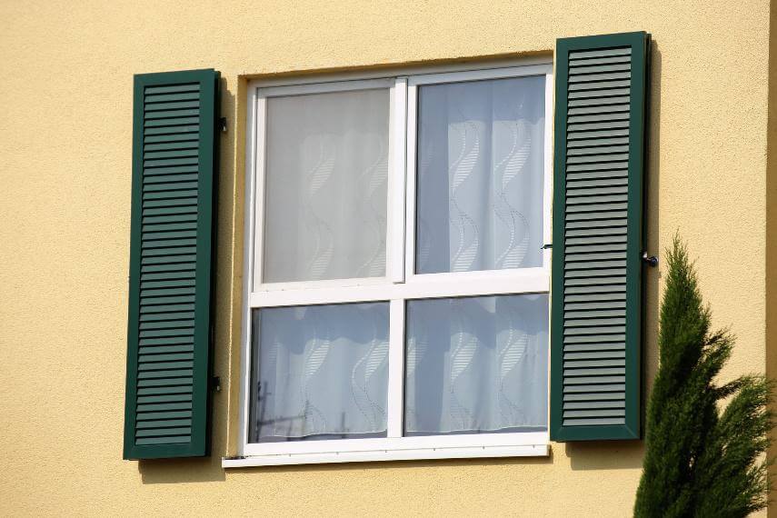 Fenster mit weißem Rahmen und zwei grünen Fensterläden an einer gelben Hausfassade