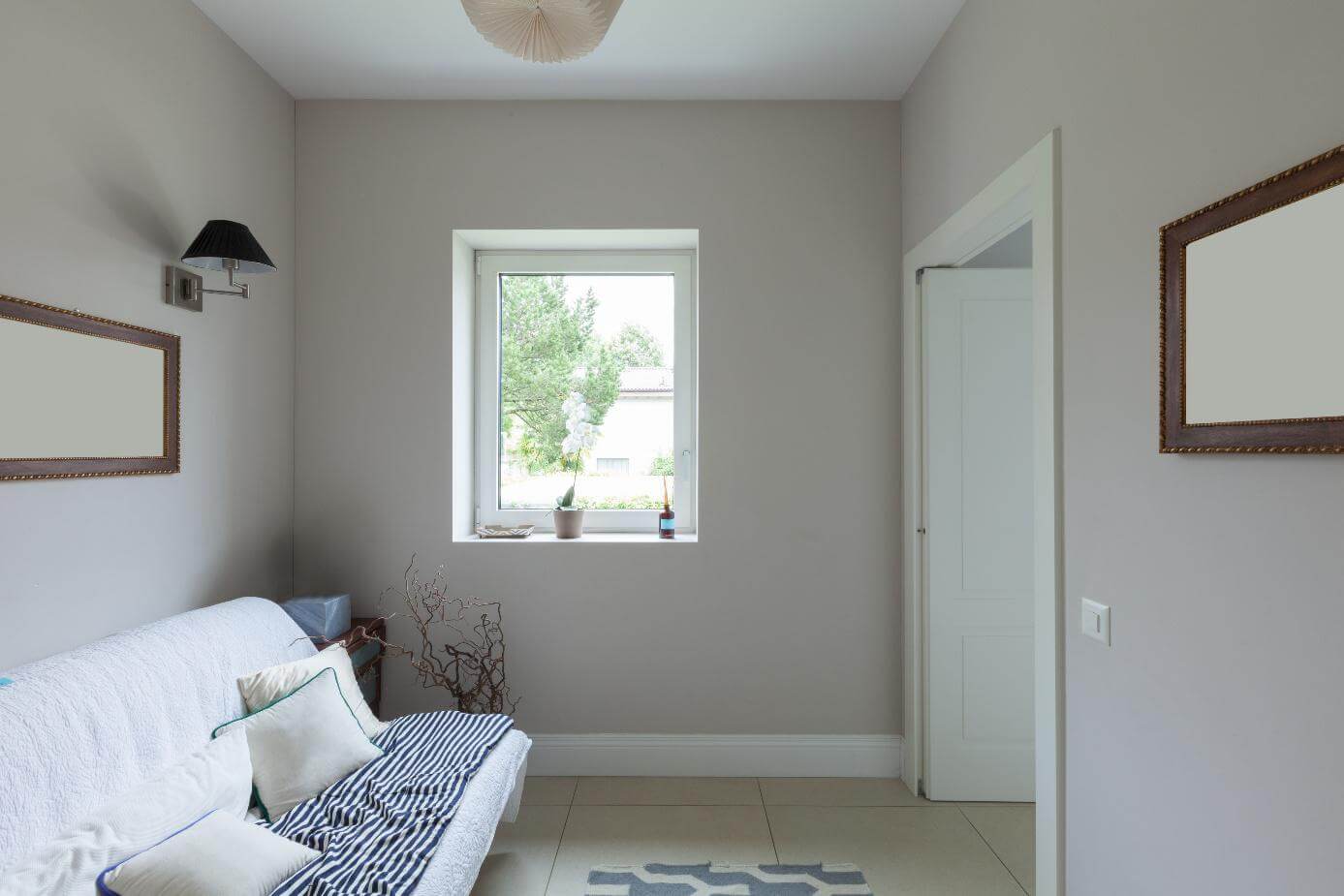 Helles Wohnzimmer mit weißem Sofa, kleinem Fenster mit Blumentopf auf der Fensterbank und schlichter Wandgestaltung.