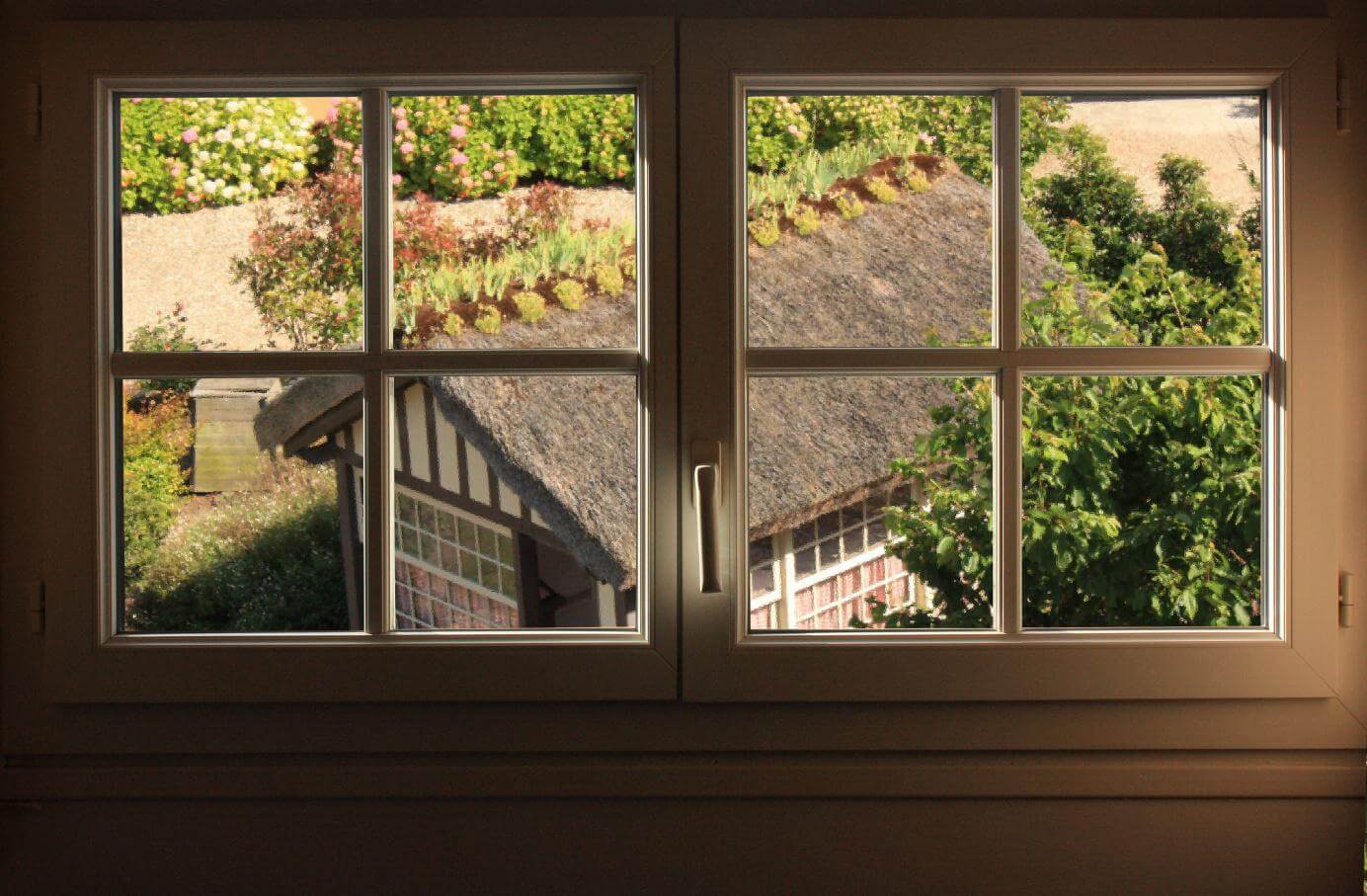 Zwei quadratische Sprossenfenster mit Blick auf Reetdach mit Garten