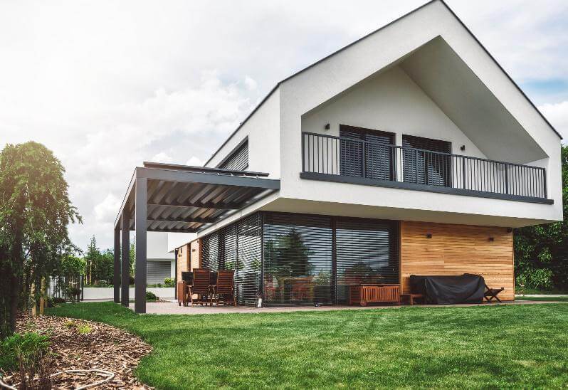 Ein zweistöckiges, modernes Haus mit einer Pergola und Garten.