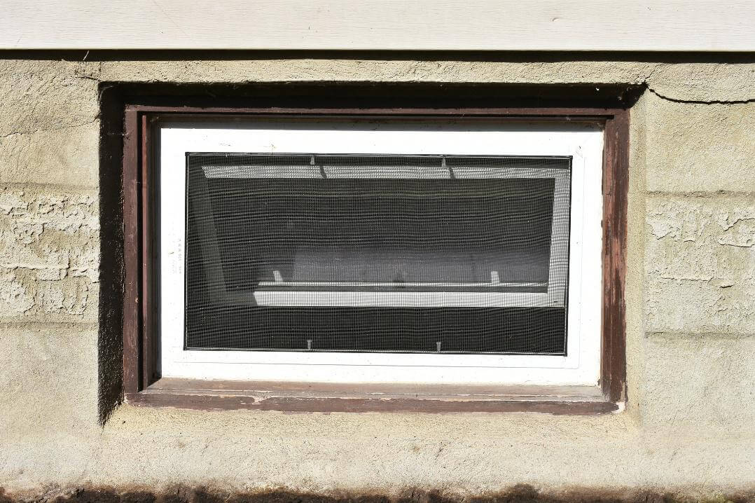 Kleines Kellerfenster mit Insektenschutzgitter in einer Betonwand