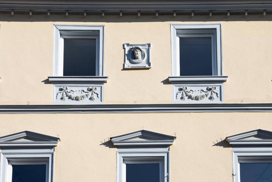 Helle Gebäudefassade mit mehreren Fenstern und dekorativen Stuckornamenten.
