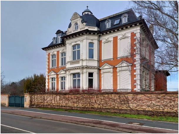 Historische Villa mit Backsteinfassade, Stuckelementen und hohen Fenstern hinter einer Mauer