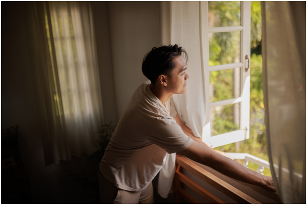 Mann guckt durch geöffnetes Flügelfenster ins Grüne.