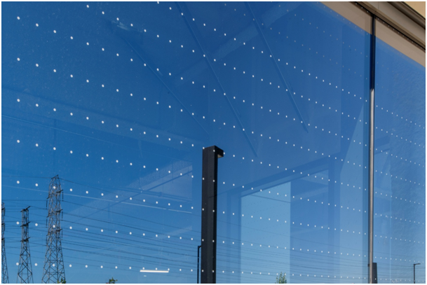 Fassade mit Fenster im Lochdesign, blauem Himmel und Metallstrebe im Hintergrund