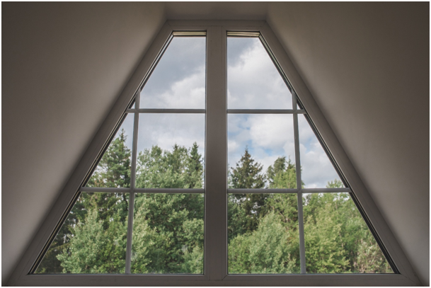 Trapezförmiges Dachfenster mit Blick auf eine Waldlandschaft und einem bewölkten Himmel
