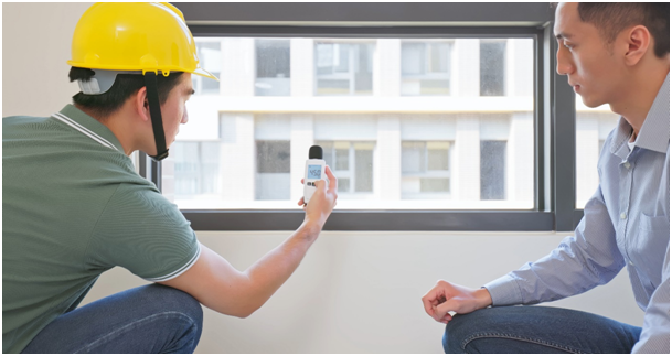 Zwei M&auml;nner hocken auf dem Boden vor einem Fenster und blicken auf ein Messger&auml;t.