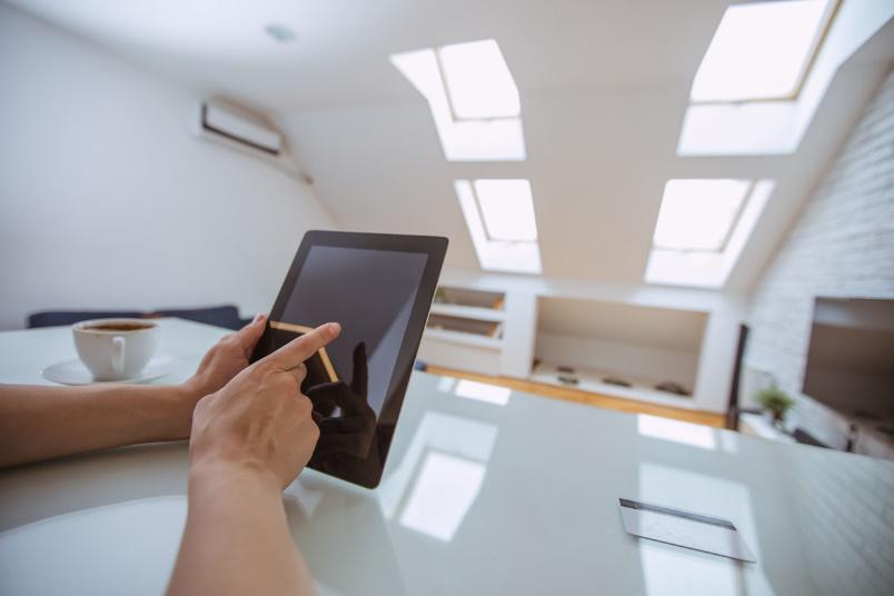 Eine Person bedient ein Tablet auf einem Tisch in einem hellen B&uuml;ro mit Dachfenstern