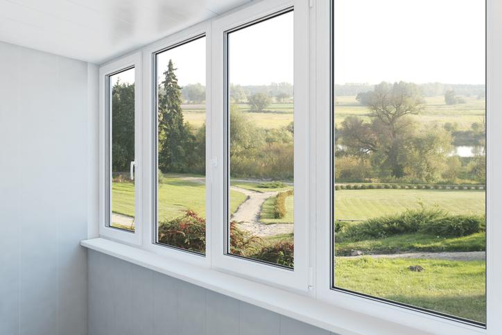Blick durch ein Fenster auf eine weite, grüne Landschaft mit einem Gehweg und Bäumen im Hintergrund.