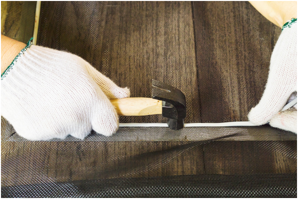Person mit Handschuhen befestigt Fliegennetz in einem Rahmen