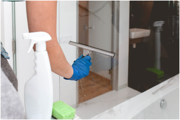 Frau mit Gummihandschuhen wischt Feuchtigkeit mit einem Fensterabzieher weg
