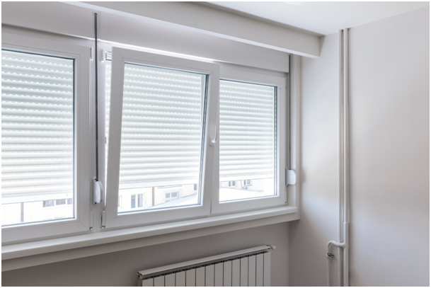 Innenansicht von drei Kunststofffenstern mit Fensteranschlägen, halb geschlossenen Rollläden und einem Heizkörper