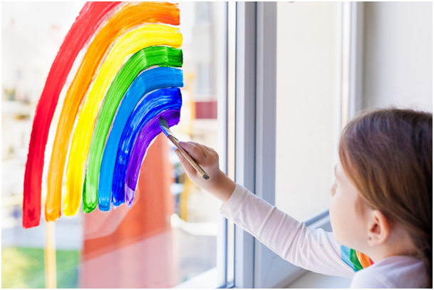Ein Kind malt einen Regenbogen mit Window Color auf ein Fenster