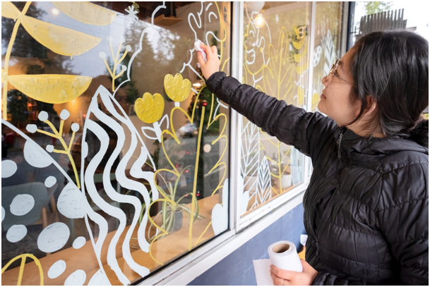 Fensterdekoration mit handgemalten floralen Mustern wird von einer Person gestaltet
