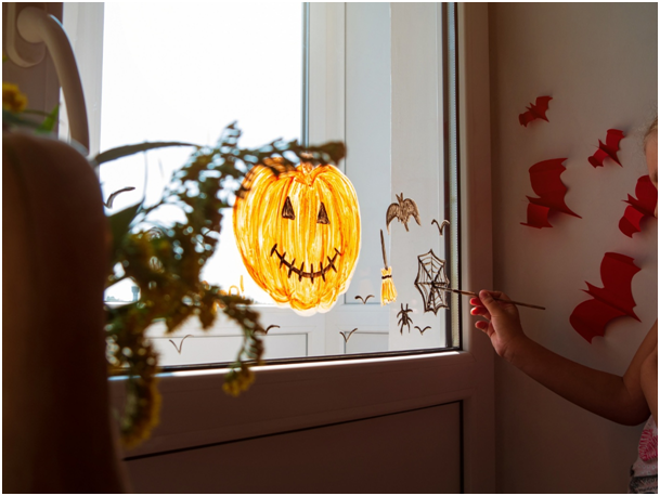 Kind malt eine K&uuml;rbisfigur, Spinnen und Flederm&auml;use sowie einen Besen auf ein Fenster