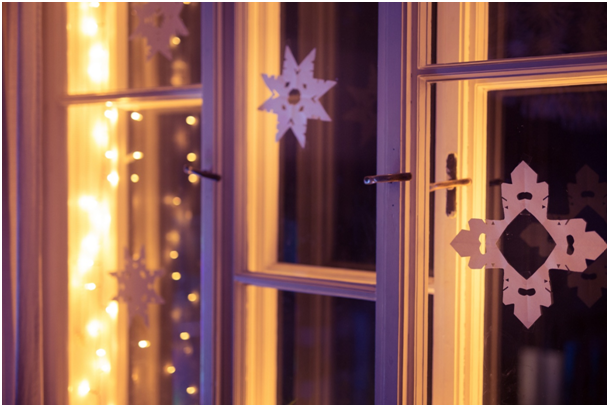 Papier-Schneeflocken an einem Fenster, das von warmen Lichterketten beleuchtet wird