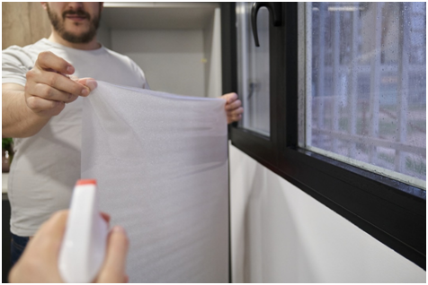 Mann bringt Fensterfolie am Fenster an, während eine zweite Person eine Sprühflasche hält