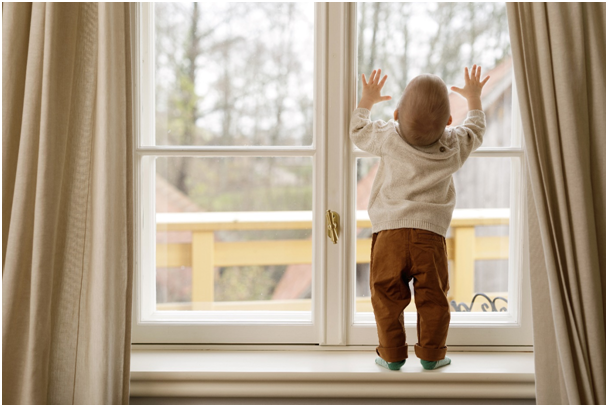 Kind steht auf der Fensterbank und drückt die Hände an die Scheibe