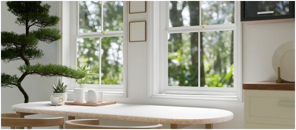 Zwei Fenster mit Sprossen vor einem minimalistischen Tisch, dekoriert mit Pflanzen und Bildern.