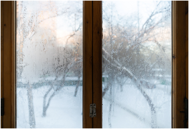 Holzfenster mit gefrorenem Glas und schneebedeckter Landschaft