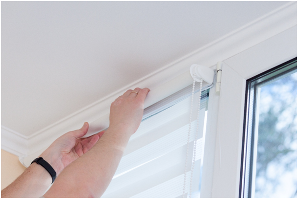 Eine Person bringt ein Rollo an einem Fenster an