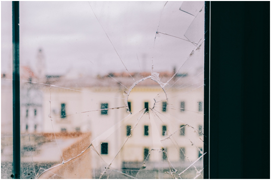 Blick aus einem Fenster mit kaputter Glasscheibe auf ein Haus gegen&uuml;ber