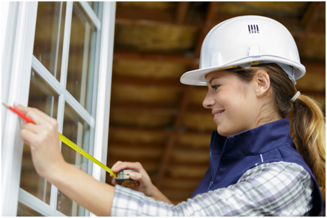 Eine gl&uuml;cklich schauende Frau misst den Rahmen eines Fensters aus