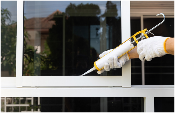 Handwerker tr&auml;gt Silikon mit einer Kartuschenpistole an einem Fensterrahmen auf