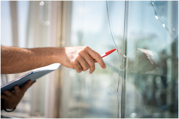 Eine Person mit einem Stift in der Hand zeigt auf einen gro&szlig;en Riss im Glas