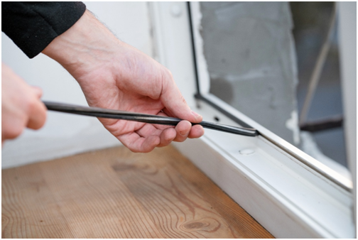 Person, die einen Fensterrahmen mit Dichtungsband abdichtet