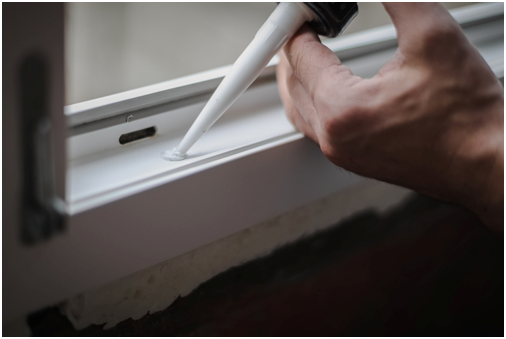 Hand dr&uuml;ckt Silikon in ein Loch im Fensterrahmen