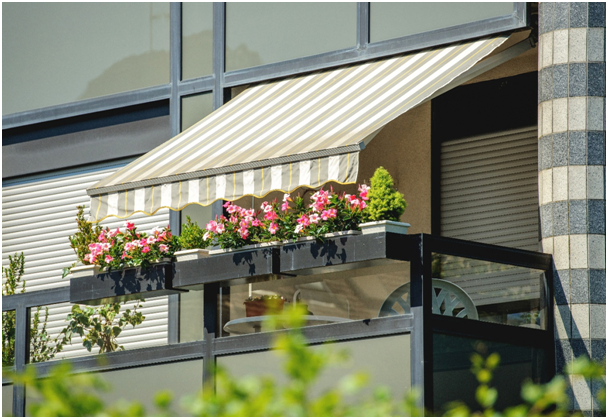 Gestreifte saubere Markise &uuml;ber einem kleinen Balkon. Dieser ist mit Blumen dekoriert.