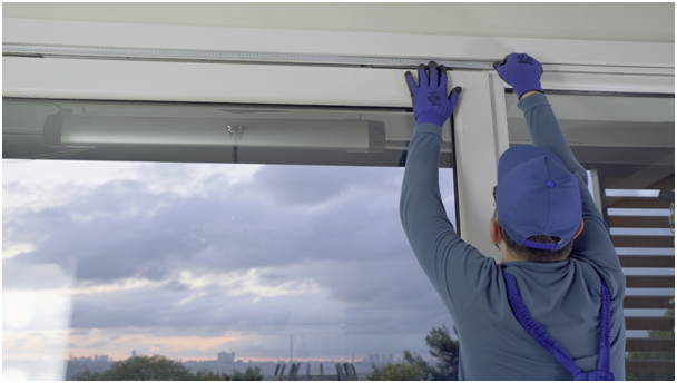 Fachkraft im blauen Overall misst Fenster von au&szlig;en mit Ma&szlig;band aus