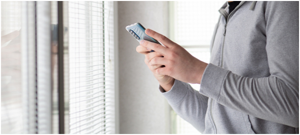 Mann steht neben smartem Fenster und benutzt sein Handy
