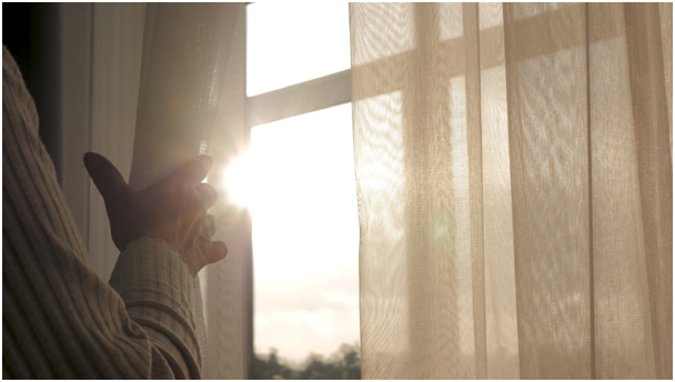 Frau &ouml;ffnet einen Vorhang und l&auml;sst die Sonne durch ein Fenster scheinen