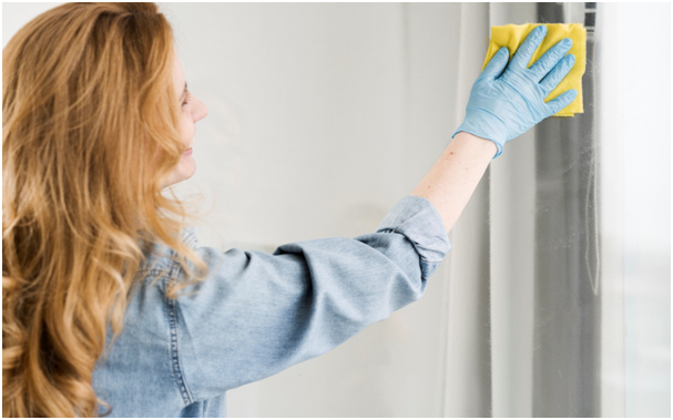 Seitenansicht einer Frau, die Fenster mit Mikrofasertuch und Handschuhen putzt