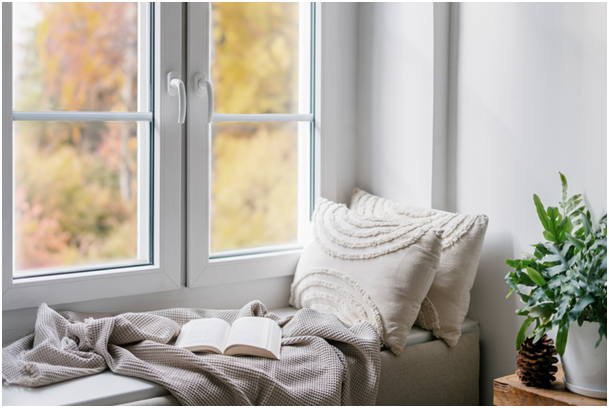 alt-Attribut: Kunststofffenster mit Fensterbank, Kissen, Decke und Buch