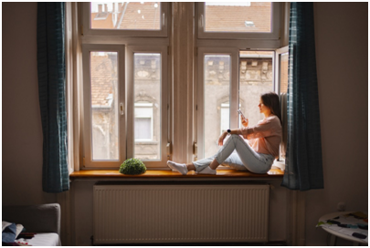 Frau sitzt mit Handy an einem Fenster.