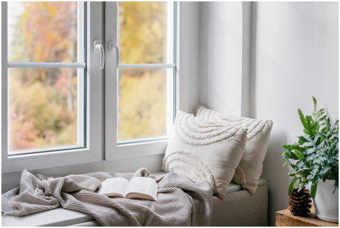 Auf einer Fensterbank liegen Kissen, eine Decke und ein offenes Buch