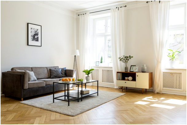 Wohnzimmer mit Sofa, Couchtisch, Sideboard und großen Fenstern mit Vorhängen