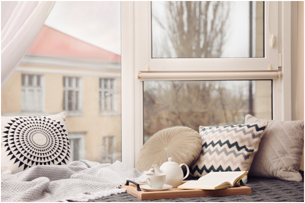 Fensterbank mit Kissen, Teekanne und offenem Buch vor einem großen Fenster