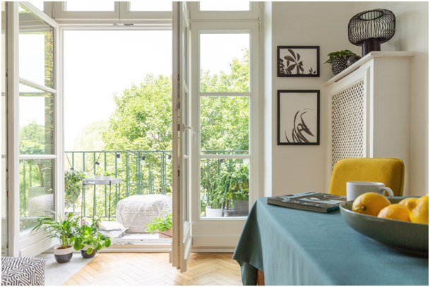 Zimmer mit Tasse, Heft und Zitronenschale auf einem Tisch sowie geöffneter Balkontür mit Pflanzen