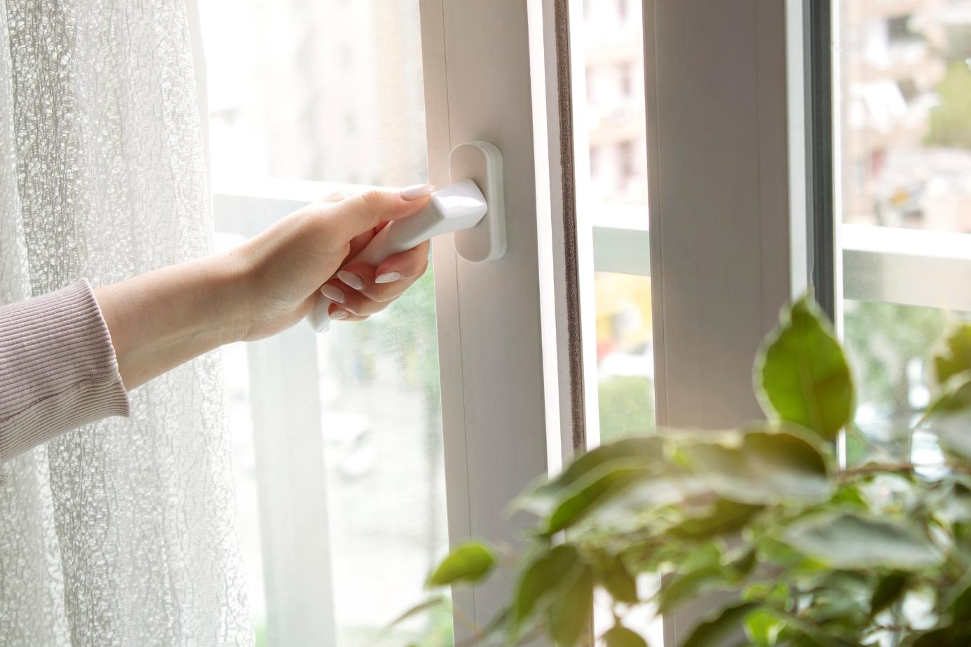 Frauenhand bedient Fenstergriff an einem modernen Kunststofffenster
