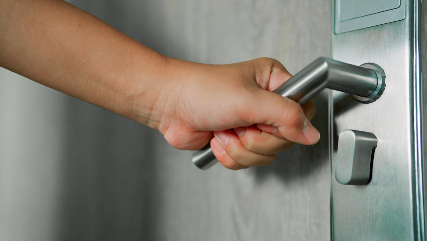Hand drückt einen modernen Metall-Türgriff an einer Innentür nach unten