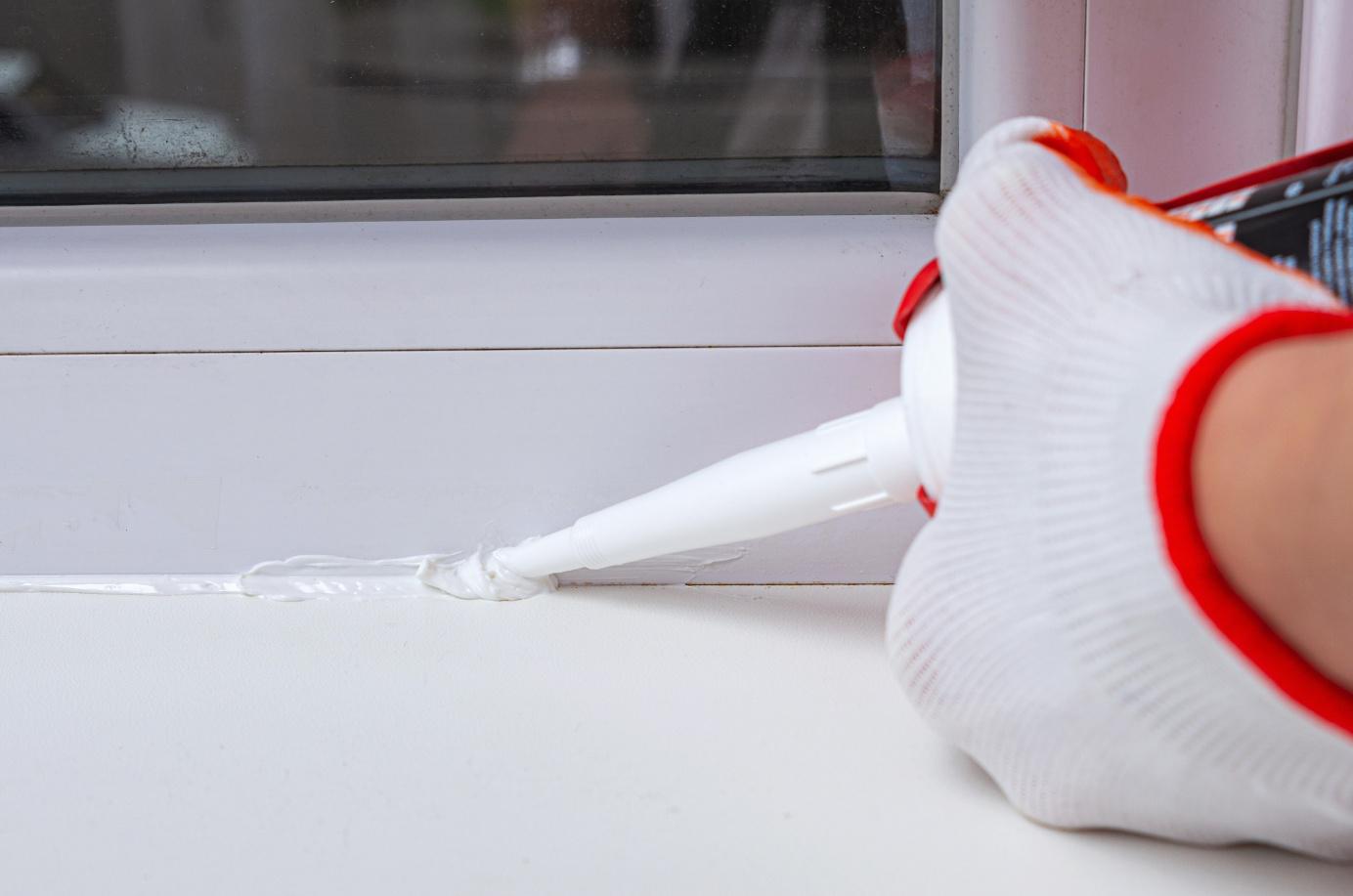 Eine Person trägt an einem Fenster neue Silikonfuge mit einer Kartusche auf
