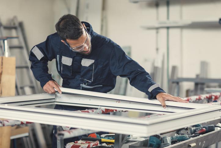 Handwerker mit Schutzbrille montiert einen Fensterrahmen in der Werkstatt.