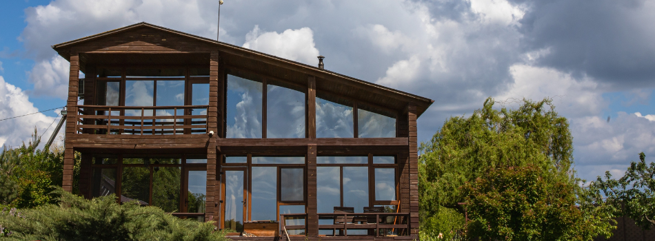 Ein modernes Holzhaus mit großen Fensterfronten von meinfesnter24, umgeben von hohen, dicht stehenden Bäumen.